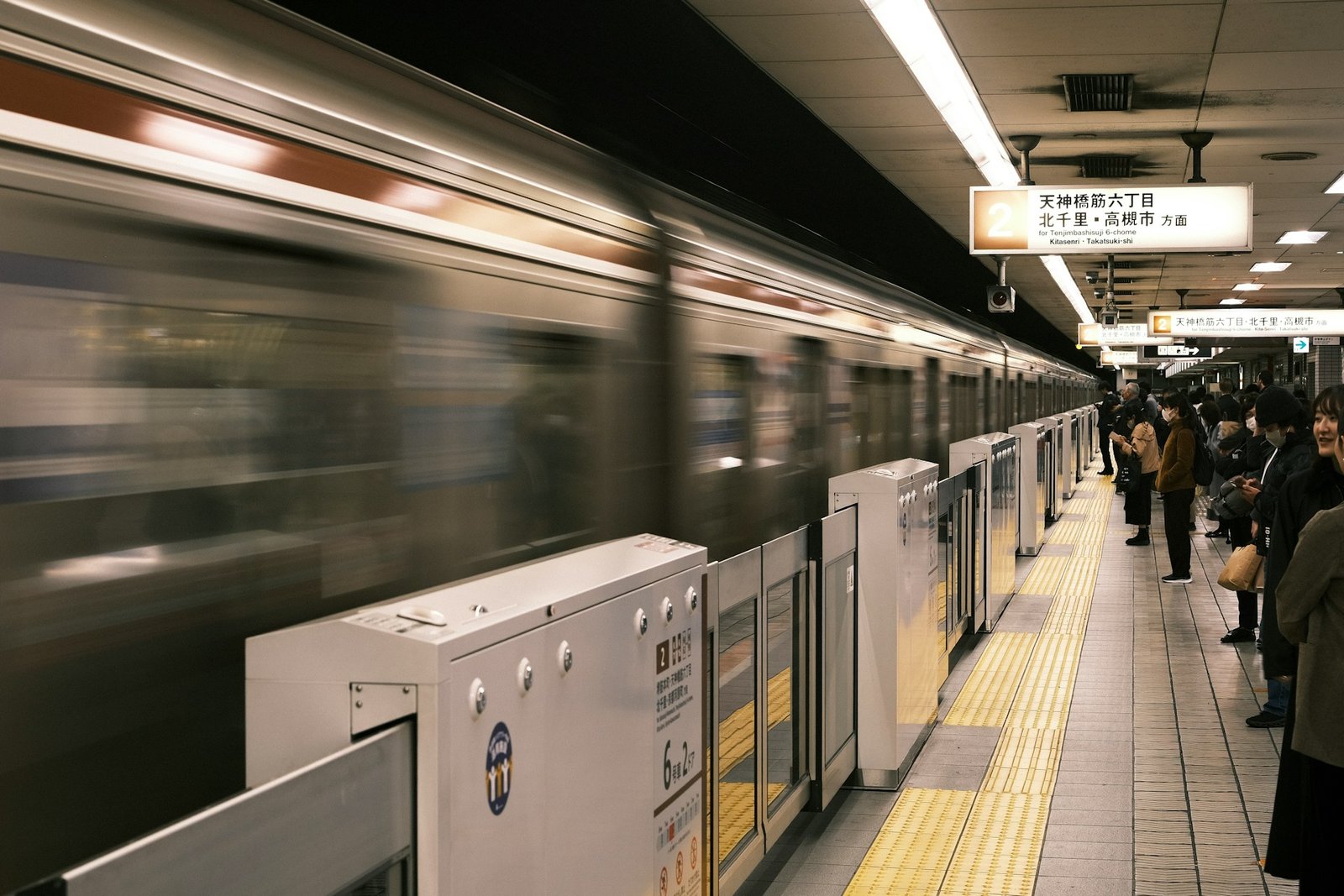 A japanese train station with a train pulling away from the platform.